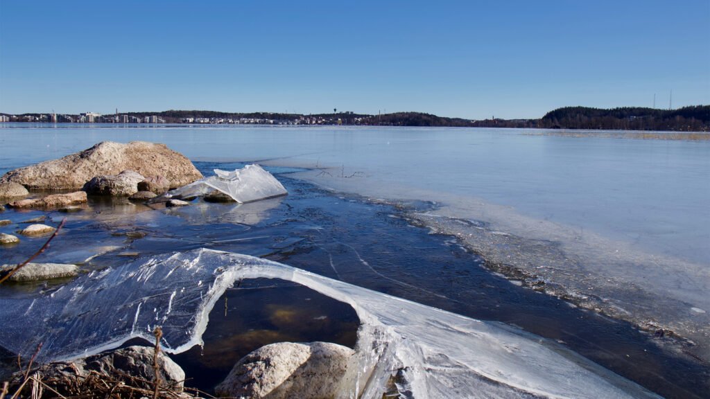 Jäitä rantakivikossa aavan järven edustalla. Horisontissa näkyy Lahden siluetti.
